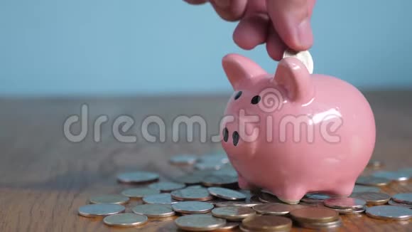 小猪银行业务站在一堆硬币的概念生活方式上一只手把硬币放在黄色的储蓄罐里视频的预览图
