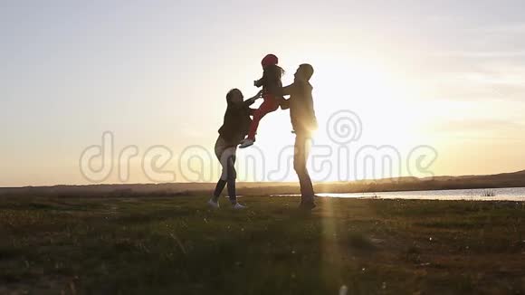 剪影和爸爸妈妈一起快乐的孩子日落时分的家人夏天快跑把孩子举起来拥抱视频的预览图