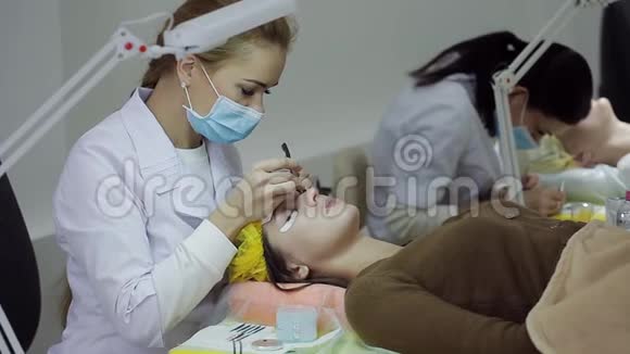 长睫毛的女人眼美容师为美容院年轻女性提供睫毛延伸视频的预览图