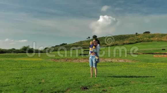 年轻的妈妈和她美丽的儿子在绿色的田野上散步阳光明媚视频的预览图