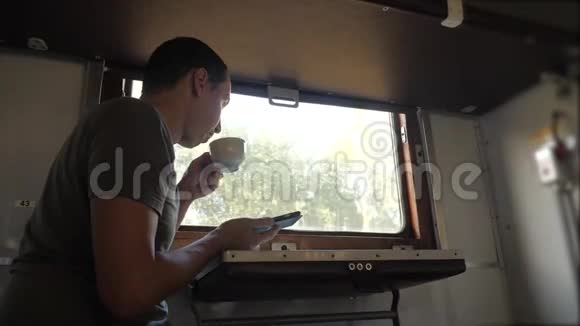 这个人坐在火车铁路车厢上拿着一部智能手机喝着咖啡的生活方式和茶慢动作视频的预览图