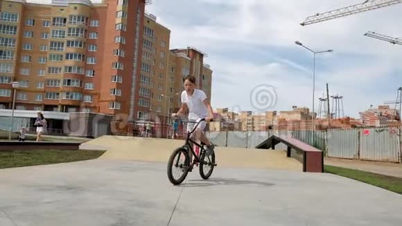 一个男孩正在阳光明媚的日子里在滑板公园骑自行车超级慢动作视频的预览图