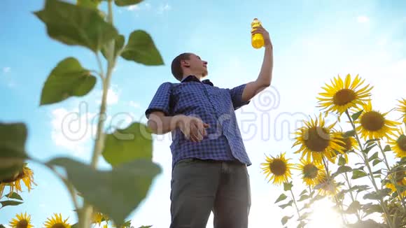 男人手里拿着一个塑料生活方式瓶葵花油站在田野里慢动作视频向日葵视频的预览图