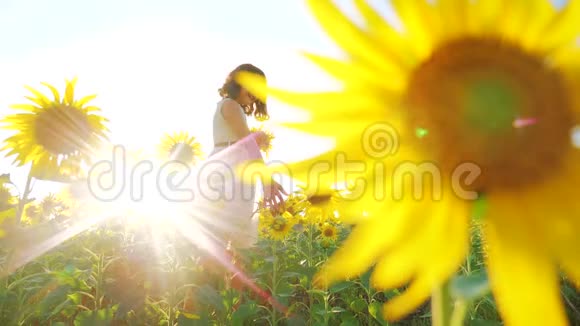 快乐的小女孩在夏天向日葵的阳光下美丽的日落小女孩向日葵慢动作视频的预览图