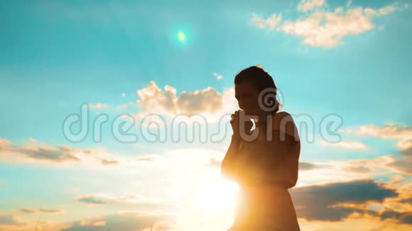 女人跪着祈祷女孩在日落时双手交叉祈祷剪影生活方式慢动作视频女孩视频的预览图