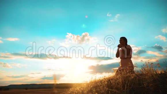 女孩在日落时双手交叉祈祷剪影女人跪着祈祷慢动作视频生活方式视频的预览图