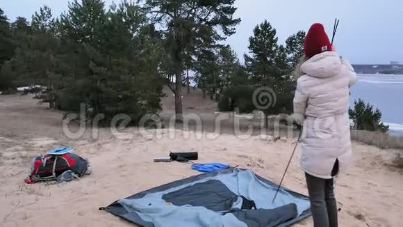 迷人的年轻旅游妇女戴着红帽子在海岸森林附近收集一个旅游帐篷视频的预览图