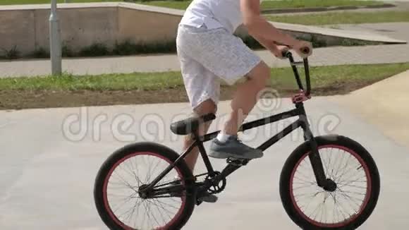 一个男孩正在阳光明媚的日子里在滑板公园骑自行车超级慢动作视频的预览图