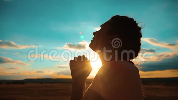 女孩在祈祷女孩在日落时交叉双手祈祷剪影慢动作视频女孩双手合拢视频的预览图