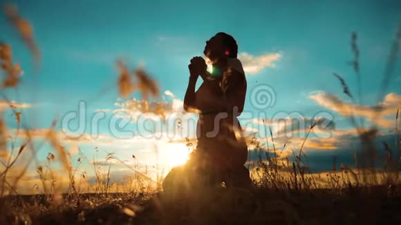 女人跪着祈祷女孩在日落时双手交叉祈祷剪影慢动作视频女孩折了起来视频的预览图