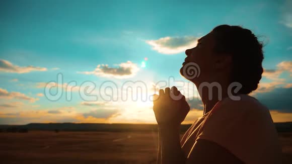 女孩在祈祷女孩在日落时交叉双手祈祷剪影慢动作视频女孩双手合拢生活方式视频的预览图