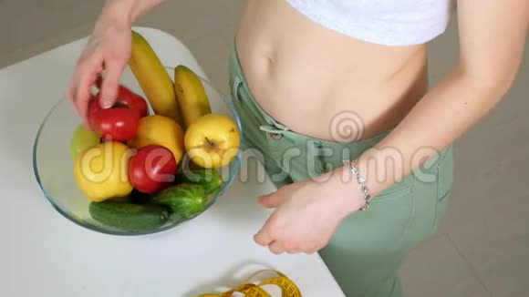 苗条的女人在一盘水果和蔬菜的背景下测量腰部这是一种健康的生活方式视频的预览图