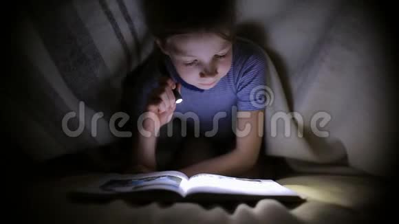 小女孩正在一个黑暗的房间里用手电筒在毯子下面看书视频的预览图