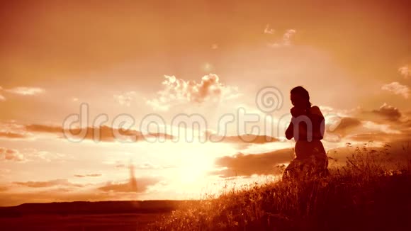 女孩在日落时双手交叉祈祷剪影女人跪在生活方式上祈祷慢动作视频女孩视频的预览图