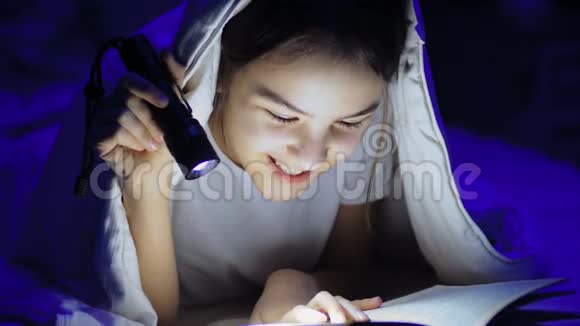 可爱的女孩躺在床上看书晚上拿着手电筒视频的预览图