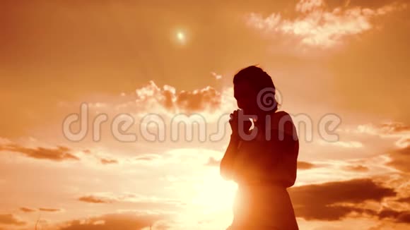 女人跪着祈祷女孩在日落时双手交叉祈祷剪影慢动作视频女孩视频的预览图