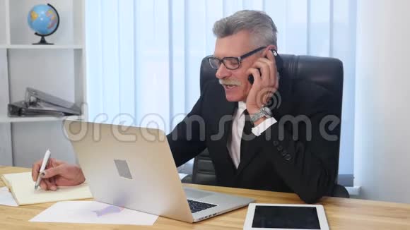 办公室里的老人用白色智能手机说话视频的预览图