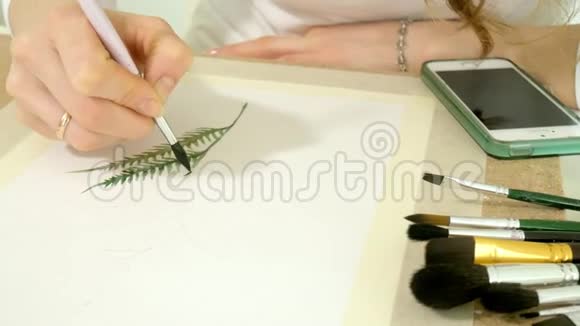 坐在桌旁一个红发的小美女用颜料和画笔作画视频的预览图