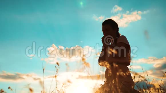 女人跪在生活方式上祈祷女孩在日落时双手交叉祈祷剪影慢动作视频女孩视频的预览图