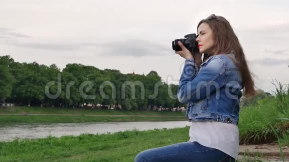 在刮风的天气里美丽的女游客用专业的照相机在河岸上拍照视频的预览图