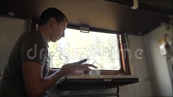这名男子坐在火车铁路车厢上手里拿着智能手机喝着咖啡和生活方式茶慢动作视频的预览图