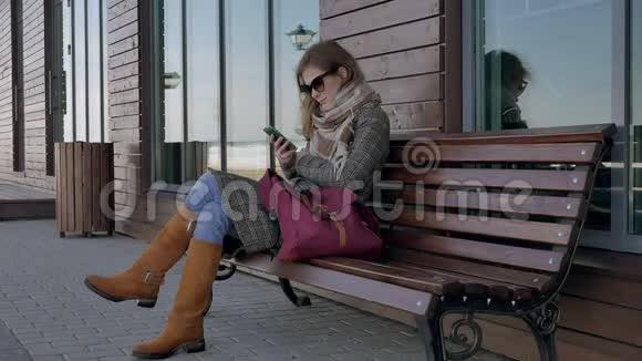 在美丽的公园里的长凳上使用智能手机放松的女人在电话展示中做手势的年轻女子视频的预览图