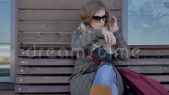 年轻美丽可爱的女人坐在公园的长凳上手里拿着她的笔记本她穿着一件外套她让她视频的预览图