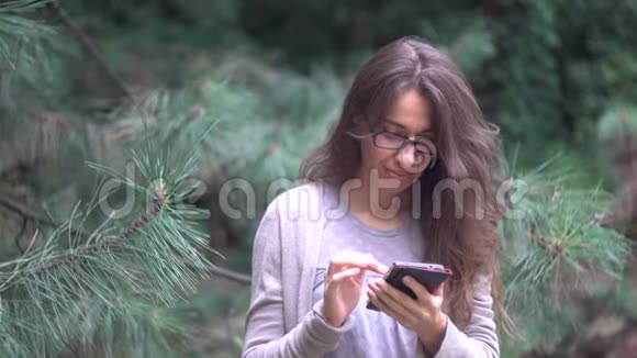 一位美丽的年轻女子在一个夏天的公园里带着智能手机视频的预览图