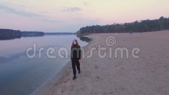穿黑色衣服的女孩在日出的海滩上散步视频的预览图