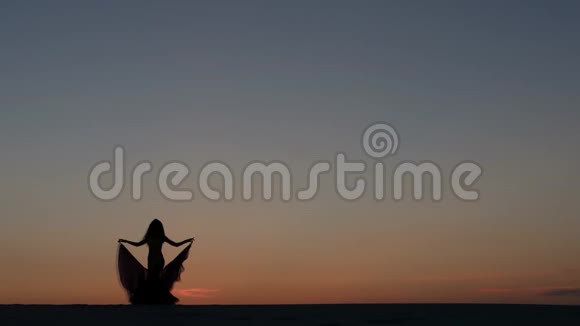 女孩在海滩上跳舞在夕阳下跳舞剪影式视频的预览图