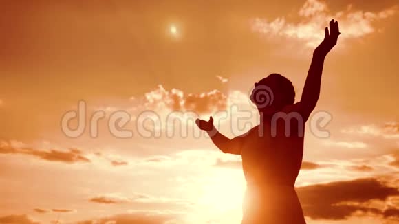 女人跪着祈祷女孩在日落时双手交叉祈祷剪影慢动作视频女孩视频的预览图