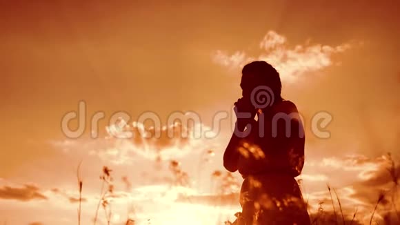 女人跪在地上祈祷生活方式女孩在日落时双手交叉祈祷剪影慢动作视频女孩视频的预览图
