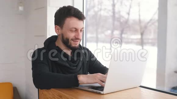 一个年轻的商人在咖啡馆的笔记本电脑前工作微笑着视频的预览图