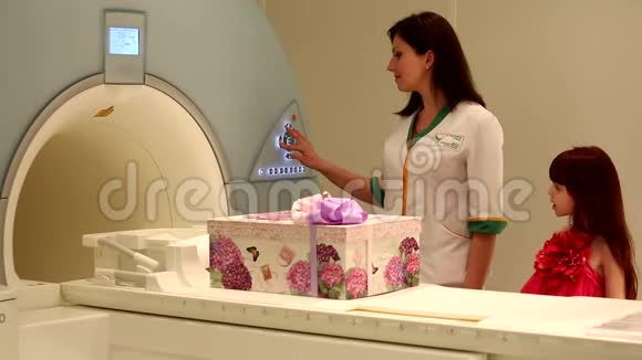 快乐可爱的小女孩和年轻的女医生看着漂亮的礼品盒在核磁共振成像机上滑动视频的预览图