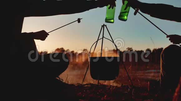 两名游客正坐在篝火晚会上在大自然中露营剪影阳光日落两个男人剪影视频的预览图