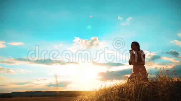 女孩在日落时双手交叉祈祷剪影女人跪着祈祷慢动作视频女孩生活方式视频的预览图