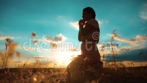 女孩在祈祷女孩在夕阳下的生活中双手合十形成祈祷的剪影慢动作视频女孩双手合十视频的预览图