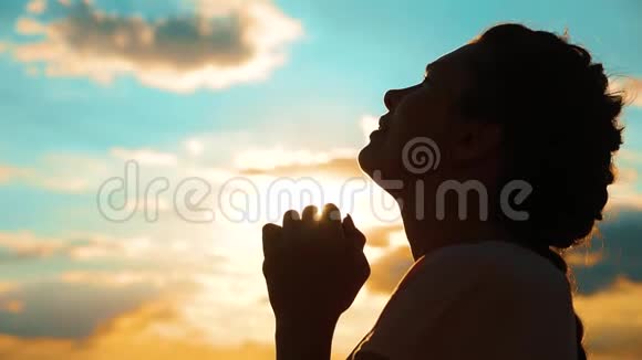 女孩在祈祷女孩在日落时交叉双手祈祷剪影慢动作生活方式视频女孩双手合拢视频的预览图