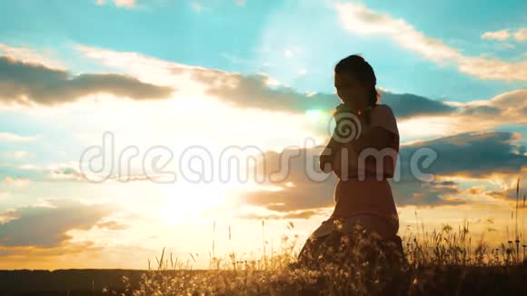 女孩的生活方式在夕阳下双手合十祈祷剪影跪着祈祷的女人慢动作视频女孩视频的预览图