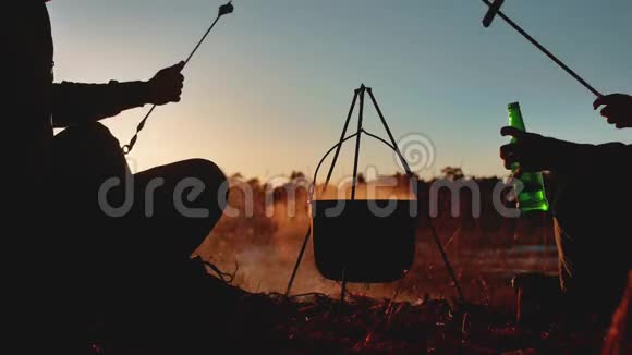 两位游客是生活方式坐在篝火旁聚会的自然野营剪影阳光日落两个男人的剪影视频的预览图