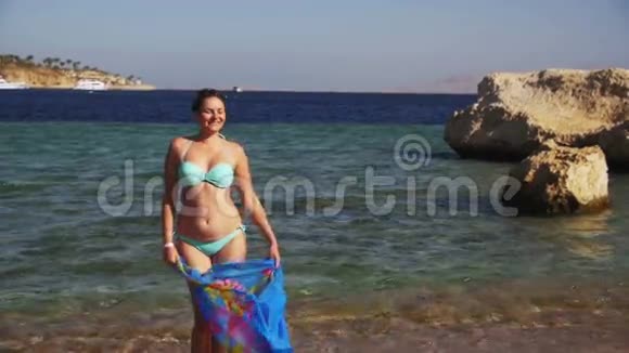 带着围巾在夏季海滩慢动作散步的快乐女人视频的预览图