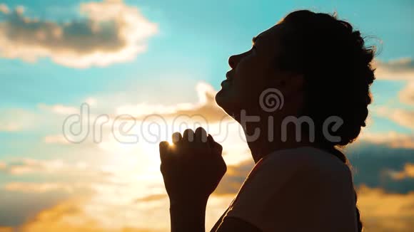 女孩在祈祷女孩在日落时双手交叉祈祷剪影慢动作视频女孩的生活方式视频的预览图