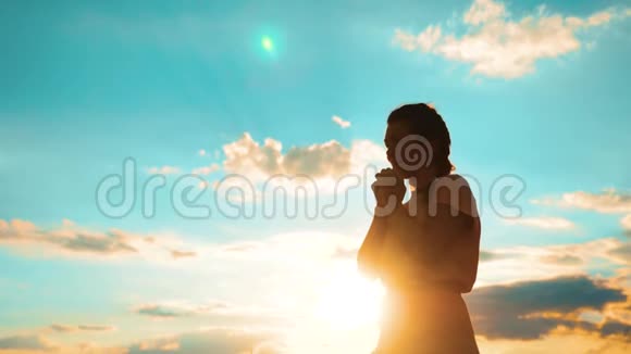 女人跪着祈祷女孩在日落时双手交叉祈祷剪影慢动作生活方式视频女孩视频的预览图