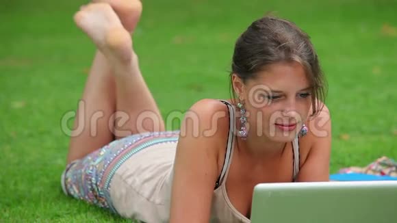 快乐的学生躺在草地上用笔记本电脑视频的预览图