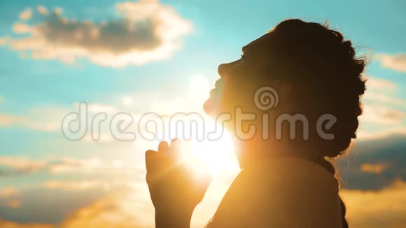 女孩在祈祷女孩在日落时交叉双手祈祷剪影慢动作视频女孩双手合拢视频的预览图