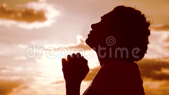 女孩祈祷女孩在日落时双手交叉在生活方式祈祷剪影中慢动作视频女孩双手合拢视频的预览图