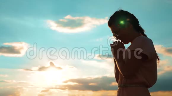 女孩在祈祷女孩在日落时交叉双手祈祷剪影慢动作视频女孩双手交叉祈祷视频的预览图