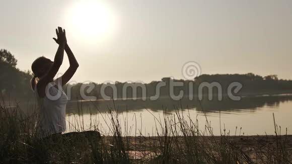 日落时分在海滩上练习瑜伽的年轻女子视频的预览图