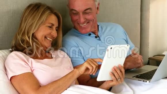微笑的情侣躺在床上用数码平板电脑视频的预览图