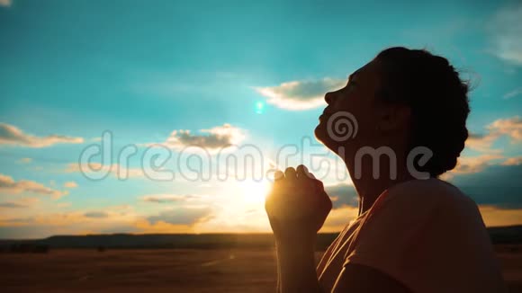 女孩在祈祷女孩在日落时交叉双手祈祷剪影慢动作视频女孩双手交叉祈祷视频的预览图